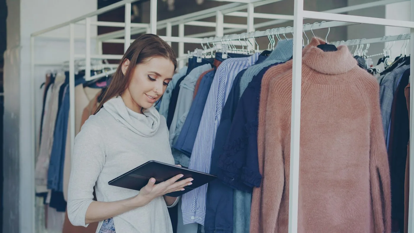 Young woman using a tablet beside clothing racks in a store.